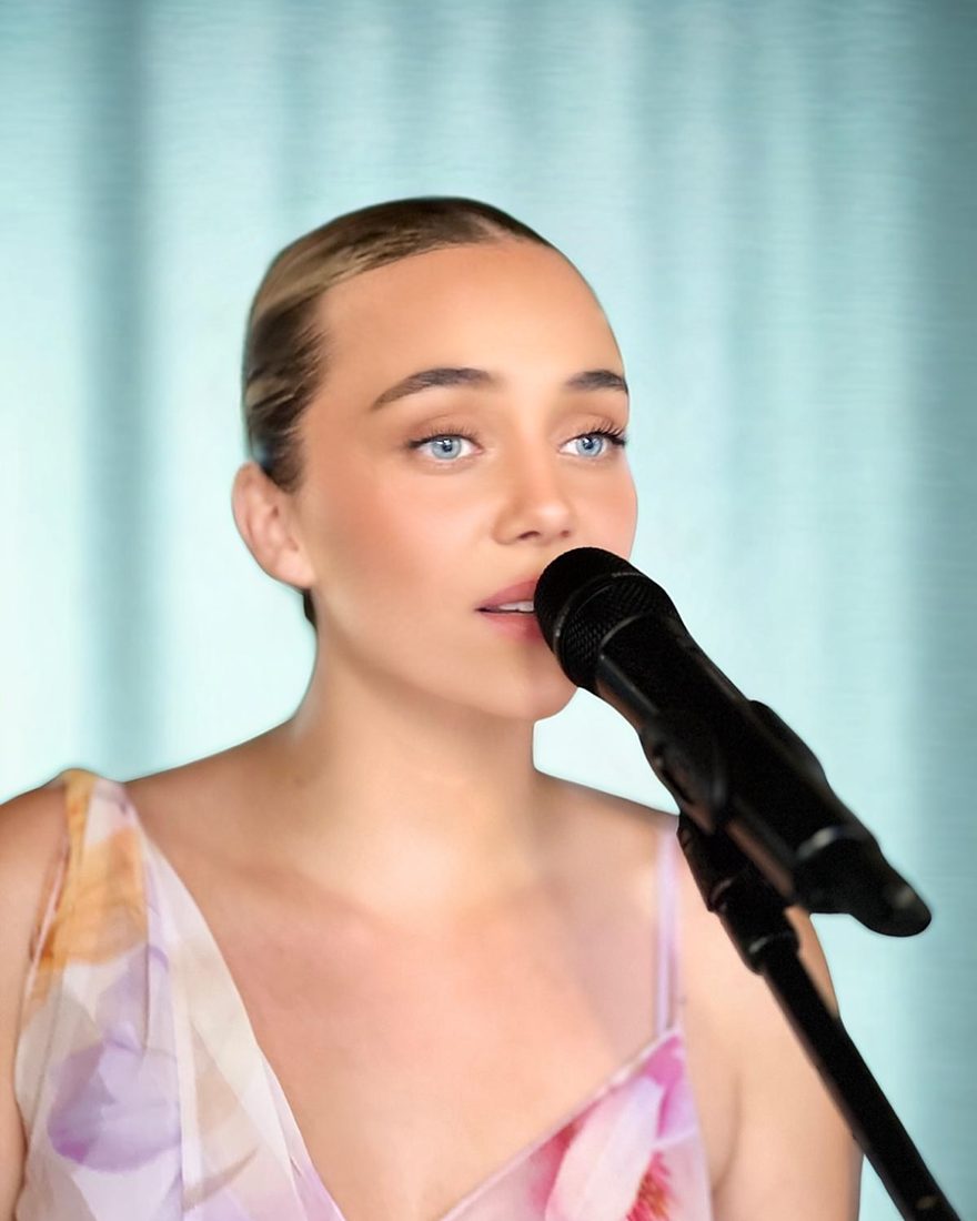 Charlotte Bard chante au micro, devant un rideau bleu clair